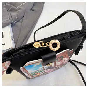 Black crossbody phone bag with cute illustration pocket, gold ring zipper, stylish daily use.
