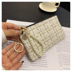 Close-up of a tweed short wallet with pearl wrist strap and gold keychain charm.
