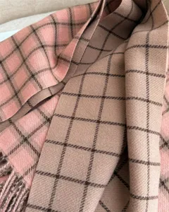 Close-up detail of the soft winter plaid scarf showing texture, pink and camel grid pattern.