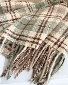 Close-up detail of cozy green and beige plaid boucle fringe scarf for autumn and winter.