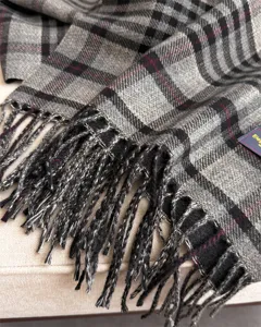 Close-up detail of grey plaid cashmere-feel scarf with fringe texture and soft woven fabric.