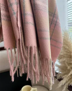 Close-up detail shot of the pink plaid cashmere-feel scarf, highlighting soft tassels.