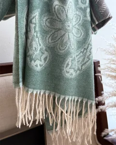 Close-up detail of a soft green patterned winter cashmere-feel shawl scarf with cute fringes.