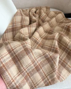 Close-up detail shot of a cozy beige and brown plaid cashmere-feel winter scarf texture.