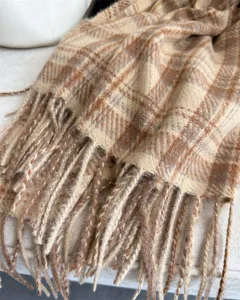 Close-up detail of a cozy faux cashmere plaid scarf with delicate fringe trim in autumn tones.