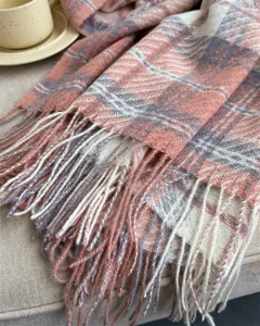 Close up of cozy winter plaid scarf detail with soft pink texture and delicate tassel fringe.