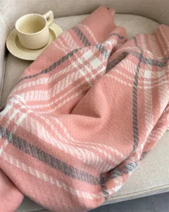 Close-up shot of a soft pink plaid scarf with cozy texture, displayed on a warm chair.