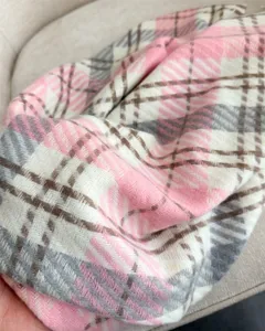 Detailed close-up of a cozy pink, grey, and white plaid cashmere-feel winter scarf.