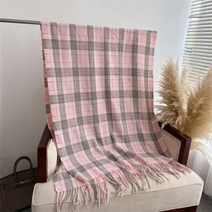 Closeup of the pink and grey plaid cashmere-feel scarf draped on a chair with fringe detail.