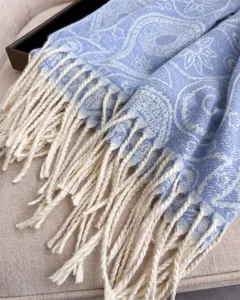 Close-up detail of blue paisley pattern winter scarf with cream twisted fringe texture.