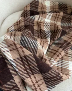 Close-up detail of soft brown plaid scarf showing fine woven fabric texture and cozy drape.