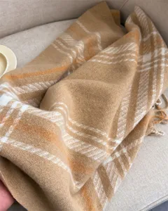Close-up detail of a soft camel and white plaid winter scarf with cozy fringe trim.