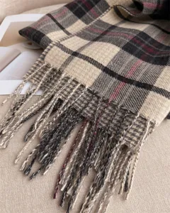 Close-up of classic plaid cashmere-feel scarf detail with soft tassels and warm texture.