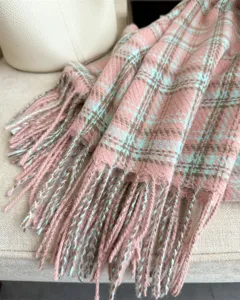 Close-up detail of soft pink blue plaid winter tassel scarf, cozy cashmere feel shawl texture.