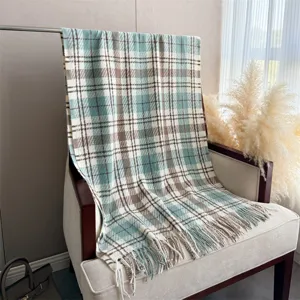 Cozy plaid blanket scarf draped on armchair, winter warm tassel shawl in soft blue and brown tones.