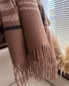 Close-up detail of soft brown plaid winter scarf with classic fringe hem and warm texture.