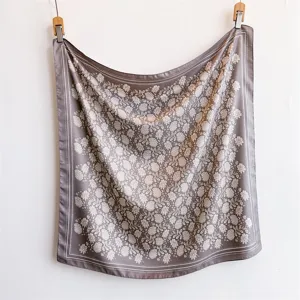 Détail d'un grand carré de soie marron à motif floral, accessoire de mode élégant pour femmes.