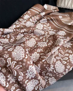 Gros plan d'un foulard en soie marron élégant orné de motifs floraux rétro raffinés.