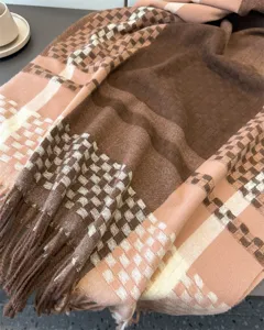 Detailed shot of soft cashmere-feel plaid scarf, warm brown and pink check pattern texture.