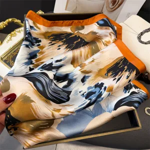 Close-up detail of luxury abstract floral printed silk square scarf with vibrant orange border.
