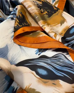 Close-up of elegant floral print silk scarf detail with vibrant orange contrast rolled edge.