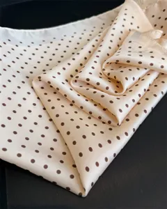 Dettaglio di sciarpa in seta con elegante motivo a pois e morbida trama su sfondo scuro.