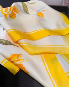 Close-up detail of luxury floral print silk scarf with elegant yellow border and fabric texture.
