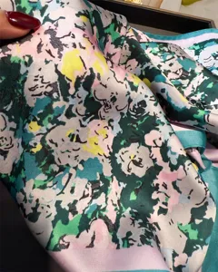 Gros-plan détail d'un foulard carré en soie imprimé coloré, motif floral abstrait.
