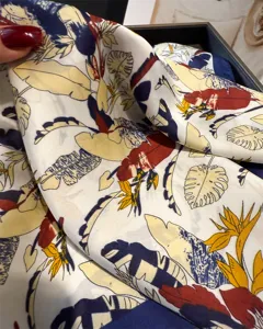 Close-up detail of a women's floral silk square scarf with colorful tropical leaf prints.