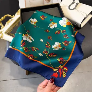 Silk scarf detail view featuring vibrant floral print, green base and contrasting blue border.