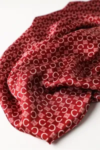 Close-up detail of red silk scarf featuring classic monogram print and soft drape texture.