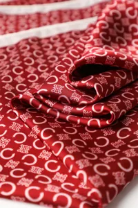 Detailed view of red silk scarf with classic monogram pattern, soft texture, elegant drape.
