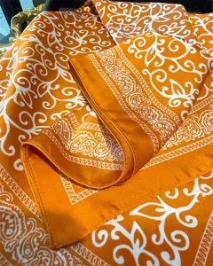 Close-up detail of orange silk-feel square scarf with classic vintage paisley and baroque print.