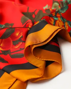 Close-up detail of luxury style red silk scarf with fruit print and gold black striped border.