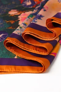 Close-up detail of smooth satin silk scarf with colorful floral print and orange border.