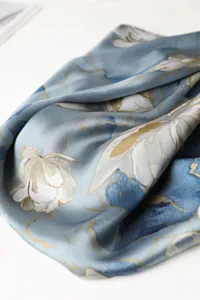 Close-up view of a blue and grey silk scarf with elegant floral print and gold line details.