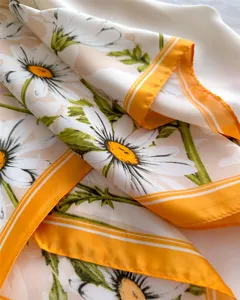 Close-up of a floral silk scarf featuring white daisies and vibrant orange border trim detail.