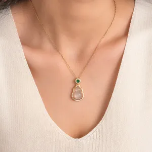Detailed view of gold-colored steel chain necklace with jade-like gourd pendant and green crystal.