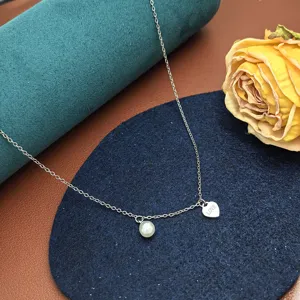 Inquadratura dettagliata di collana minimalista in acciaio titanio con perla e cuore.