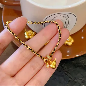 Close-up detail of a stylish gold braided bracelet featuring delicate gourd and floral pendants.