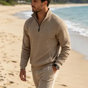 Detailed view of a stylish men's waffle knit quarter-zip sweatshirt in khaki on a beach.