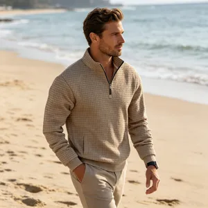 Detail shot of men's beige quarter-zip stand-up collar waffle knit sweatshirt in beach scene.