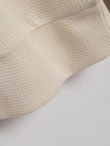 Primo piano dettagliato di tessuto a maglia waffle beige, che mostra consistenza e traspirabilità.