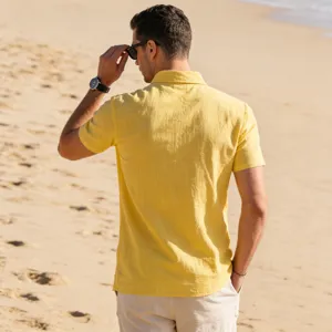 Casual men's yellow linen short-sleeve shirt worn outdoors on beach, detailed lifestyle view.