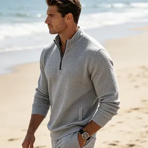 Detail shot of men's grey textured quarter zip sweatshirt on beach, casual knitwear.