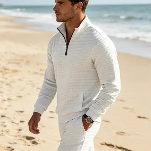 Detailed view of men textured grid quarter-zip sweatshirt and pants on beach lifestyle backdrop.