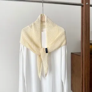 Detailed view of the cream hollow knit triangular shawl scarf hanging on a wooden hanger.