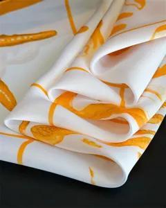 Close-up detail shot of elegant white silk scarf featuring vibrant orange artistic print texture.