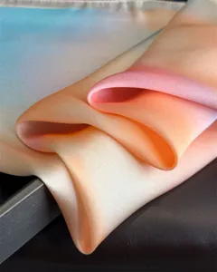 Close-up detail of a soft gradient silk scarf with elegant folds and peach and blue tones.