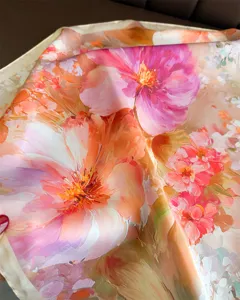 Gros plan détaillé d'un foulard carré en satin imprimé de fleurs roses et oranges.